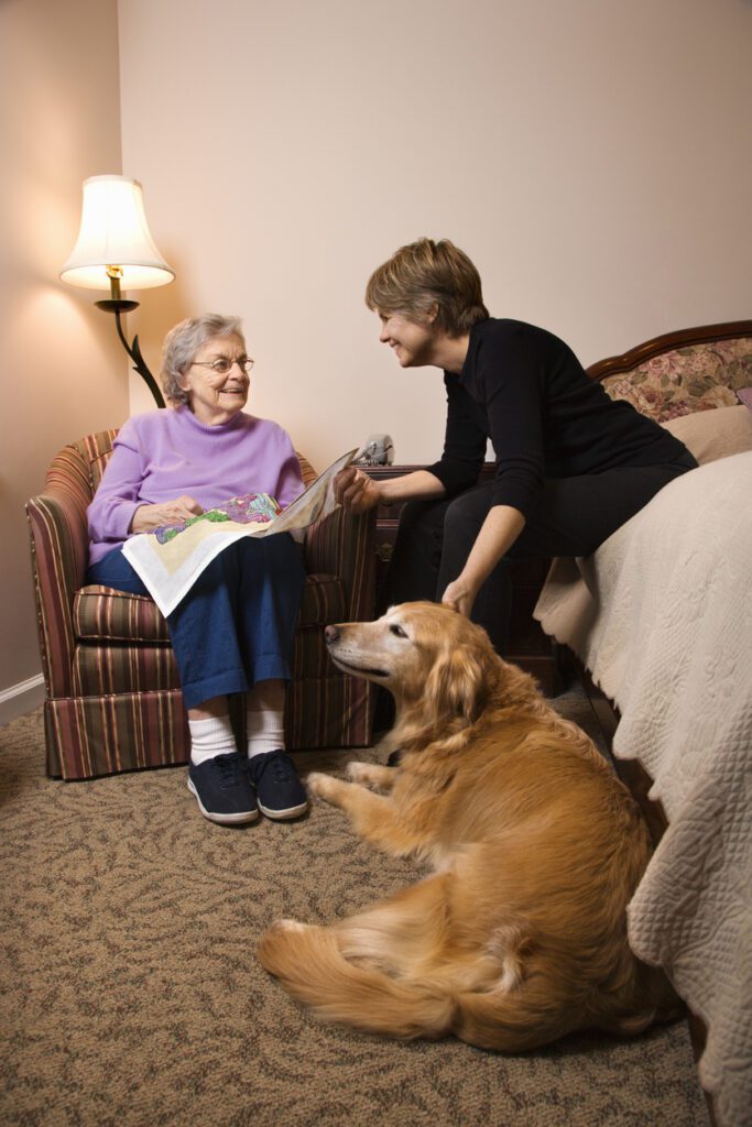 A woman sitting on the floor with an older person and a dog.